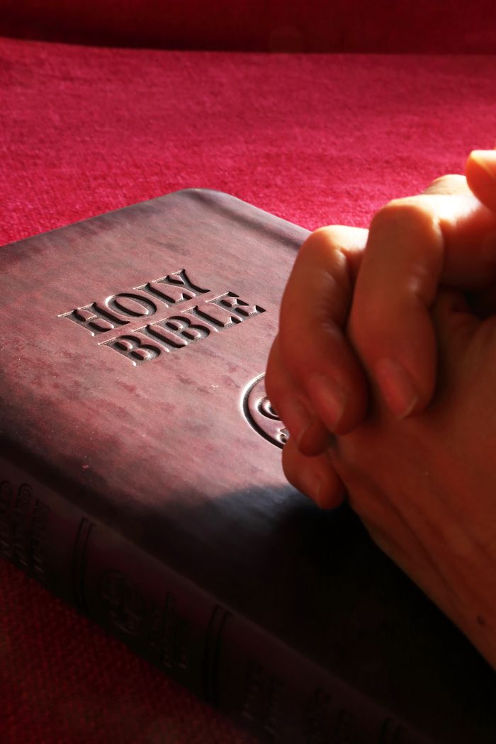 Offerings Close-up of hands praying on a Holy Bible, symbolizing faith and spirituality.